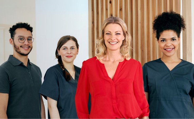 Drei junge Frauen und ein junger Mann stehen nebeneinander und Blicken in die Kamera