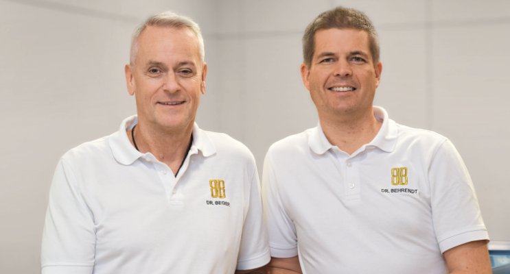 Zwei Männer in weißen Polohemden stehen nebeneinander uns blicken in de Kamera.