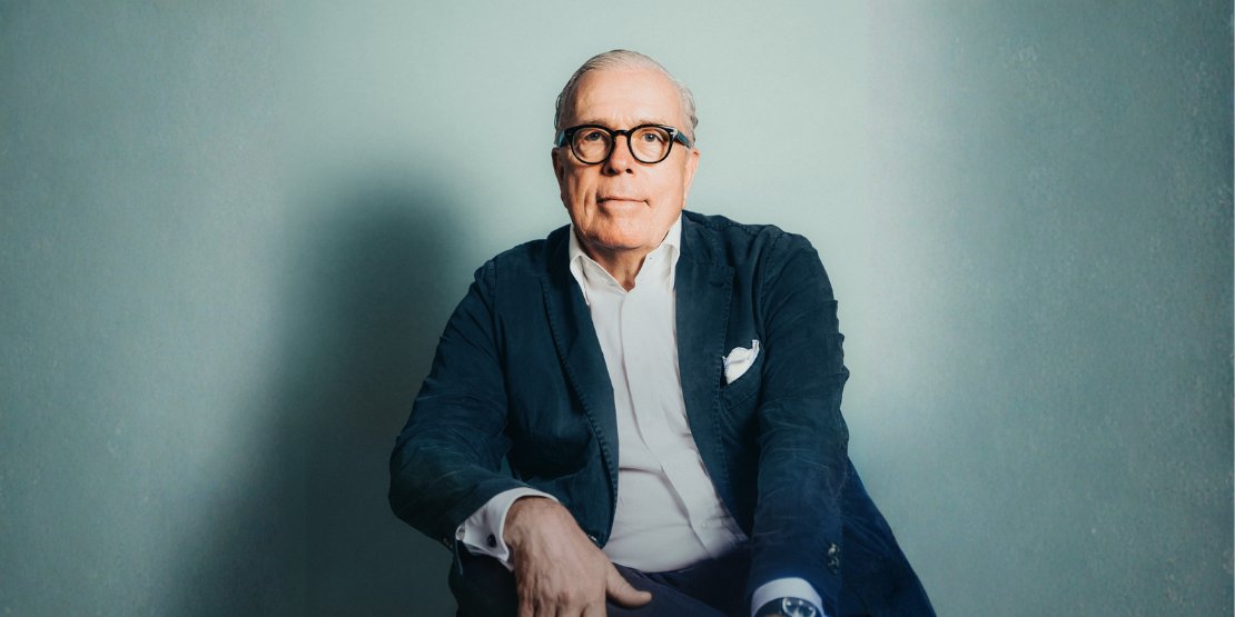 Mann mit blauem offenen Hemd und dunklem Jacket schaut in die Kamera