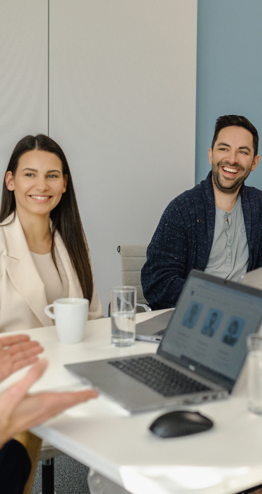 Mehrere junge Personen sitzen in einem Meeting und besprechen lächelnd Business Thematiken.