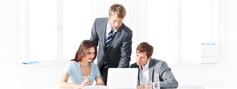 Eine junge Frau und zwei Männer in Anzug sitzen vor einem Laptop